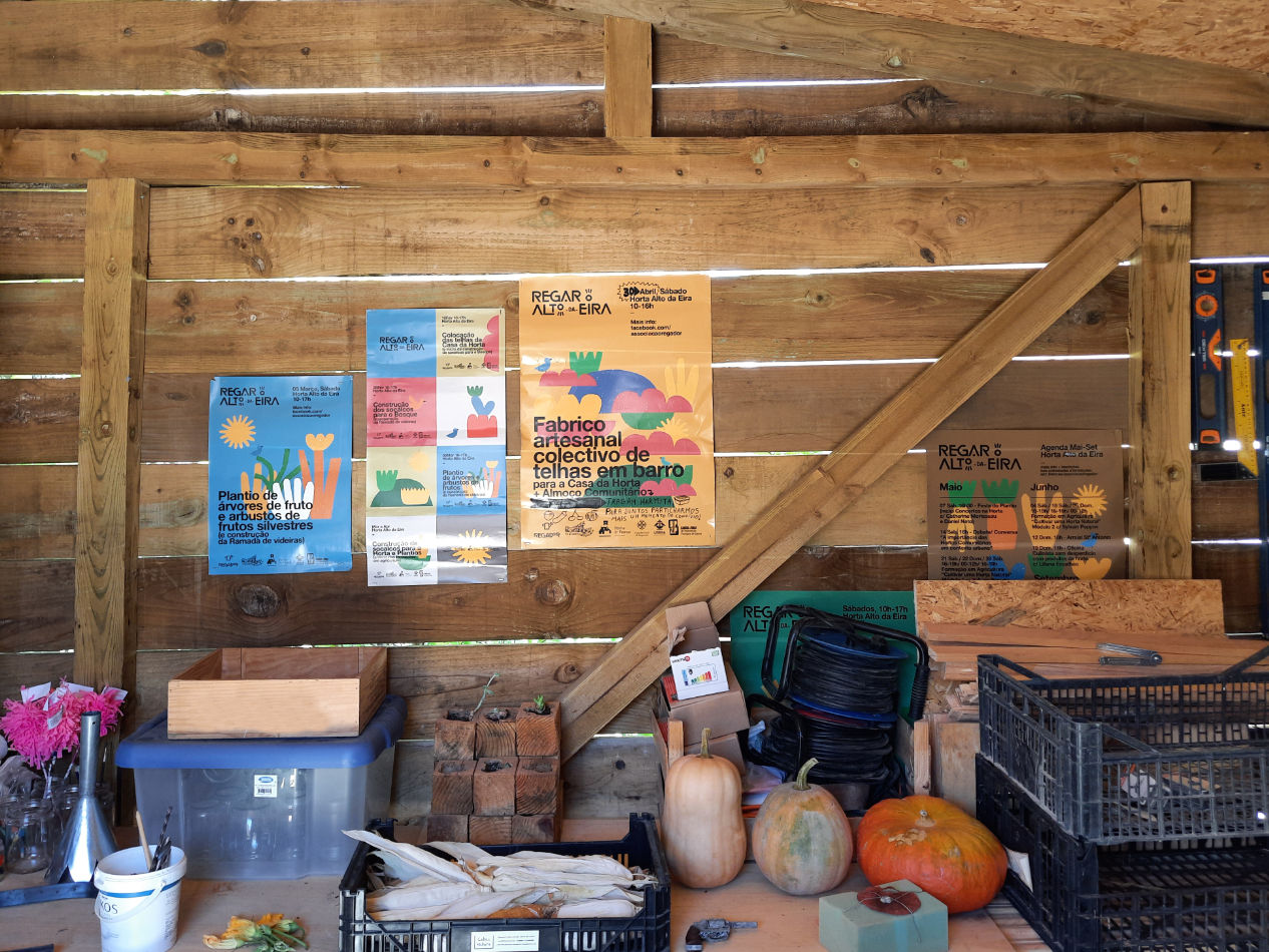 Fotografia dos cartazes de eventos da Associação Regador, expostos na parede da sala da horta, mostrando a aplicação física da comunicação gráfica.
