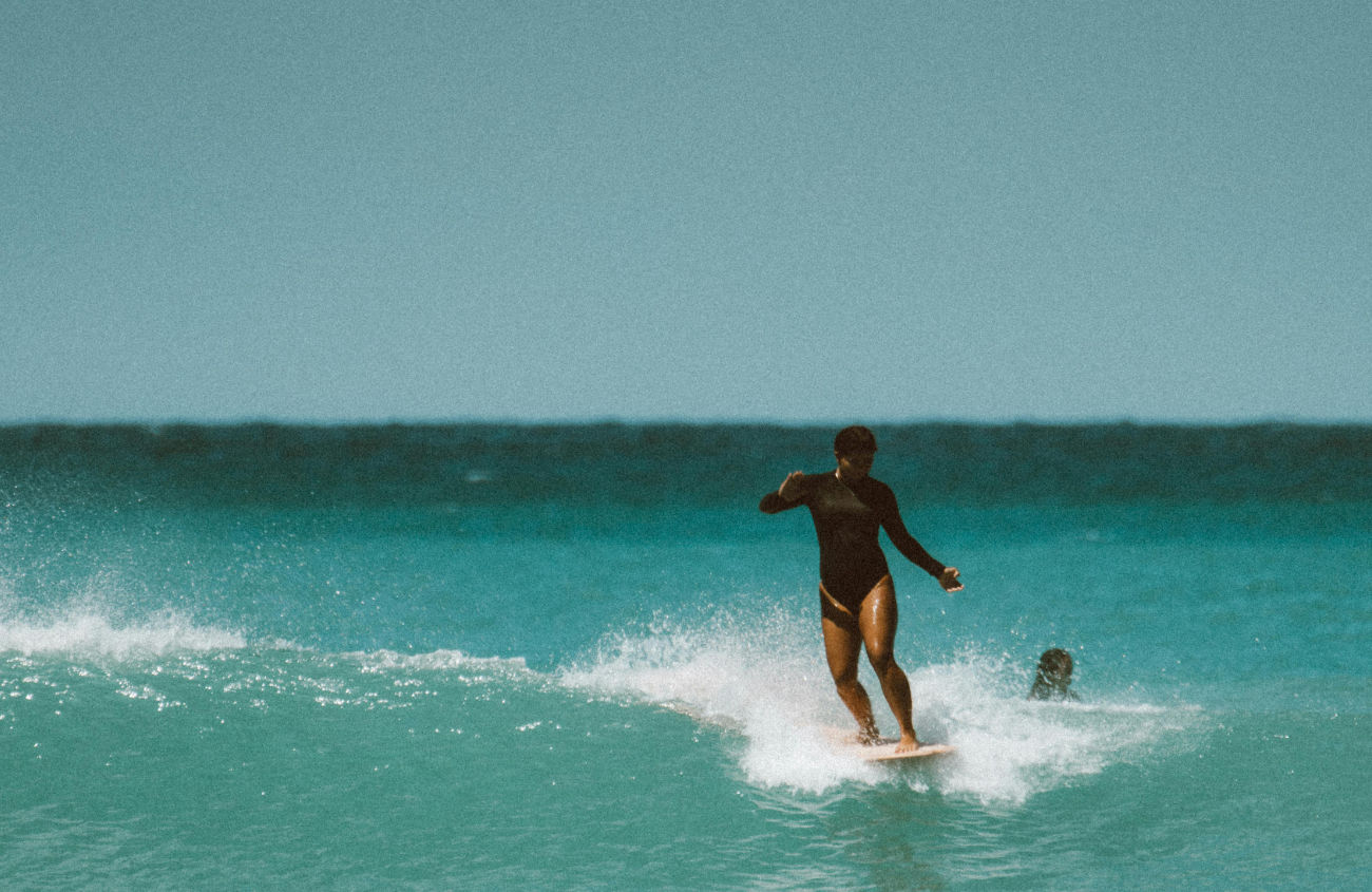 Uma surfista no oceano, a deslizar numa onda, personificando a sensação de liberdade e fluidez que está no centro da filosofia da A NEW DAY